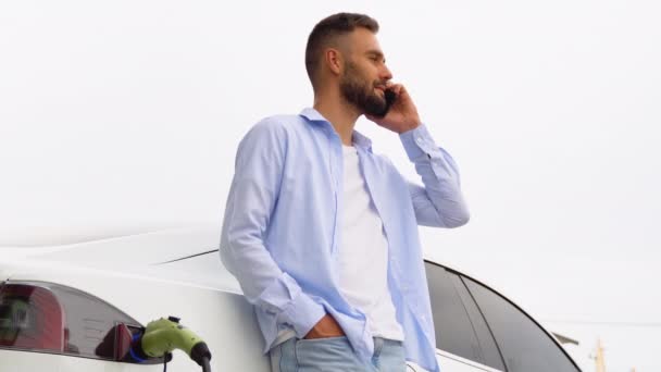 Een Man Aan Telefoon Tijdens Het Opladen Van Auto Bij — Stockvideo