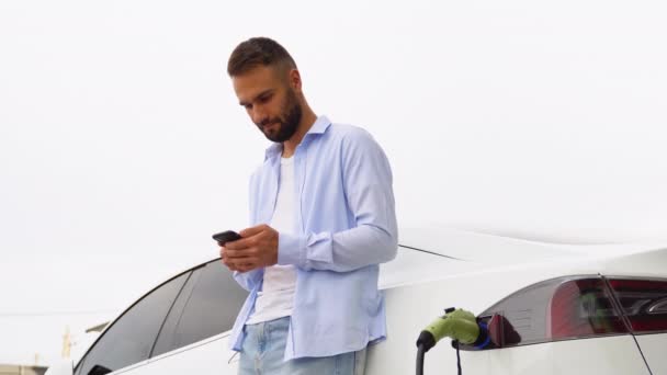 Homem Barbudo Usa Aplicativo Móvel Para Controlar Bateria Carro Elétrico — Vídeo de Stock