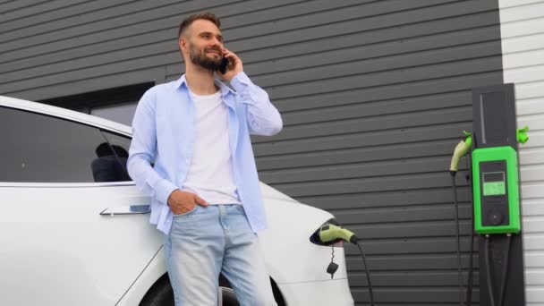 Mężczyzna Rozmawiający Przez Telefon Podczas Ładowania Luksusowego Samochodu Elektrycznego Stacji — Wideo stockowe