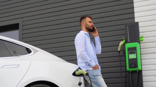 Elektrikli Taşıt Şarj Istasyonunda Bir Adam Araba Şarj Ederken Telefon — Stok video