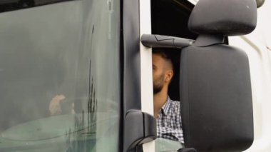 Bir sürücü açık pencereden kameraya bakarken kamyonun içinde oturuyor..