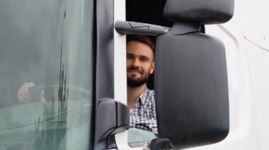 Bir sürücü açık pencereden kameraya bakarken kamyonun içinde oturuyor..