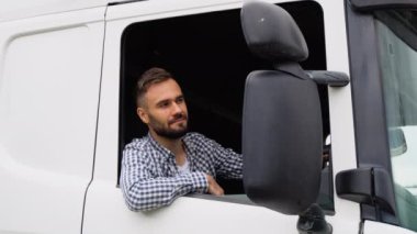 Bir sürücü açık pencereden kameraya bakarken kamyonun içinde oturuyor.