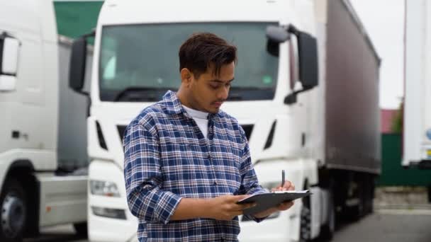 配送倉庫の駐車場に立っている間郵送物リストを点検するトラック運転手 — ストック動画