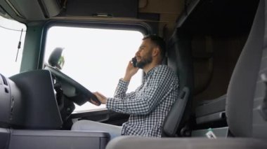 Kamyon şoförü kamyonetinin kabininde otururken cep telefonuyla konuşuyor. Sağ el sürücüsü araba..