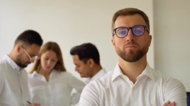 Kendinden emin iş adamı lideri takım toplantısında ofiste kameraya bakıyor..