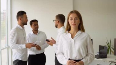 Gülümseyen, kendine güvenen iş lideri kameraya bakıyor ve takım toplantısında bir ofiste duruyor..