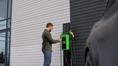 Bir adam elektrikli arabayı şarj etmek için mobil uygulama kullanıyor..