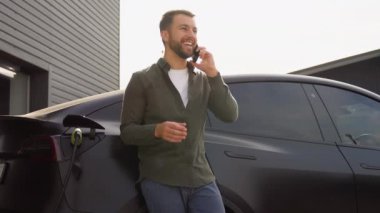 Elektrikli araç şarj istasyonunda araba şarj ederken yakışıklı bir adam telefon ediyor..