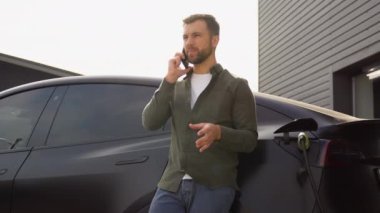 Evin yakınında elektrikli araba şarj ederken telefon eden yakışıklı bir adam..