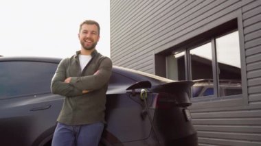 Şarj istasyonunda arabayı şarj ettiği için duran bir adam.