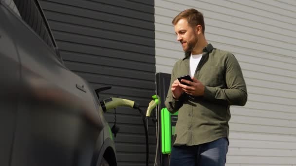 Man Som Använder Smarttelefon Och Laddar Bilen Fordonets Laddningsstation — Stockvideo