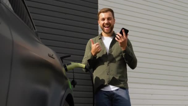 Szczęśliwy Człowiek Telefonem Podczas Ładowania Samochodu Elektrycznego Stacji Ładowania Pojazdów — Wideo stockowe