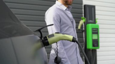 Adamın biri şarj kablosunu elektrikli bir arabaya bağlayıp kapatıyor..