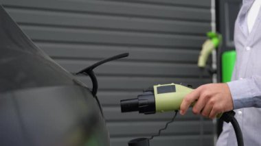 Bir adam elektrik kablosunu elektrikli bir arabaya bağlar..