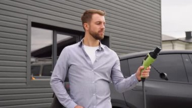 Elektrikli araba şarj istasyonunda şarj aleti olan gülümseyen adam..