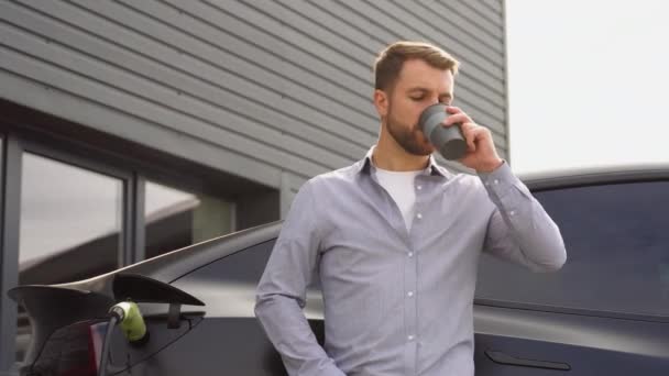 Handsome Man Charging Electric Car Drinking Coffee — Stock Video