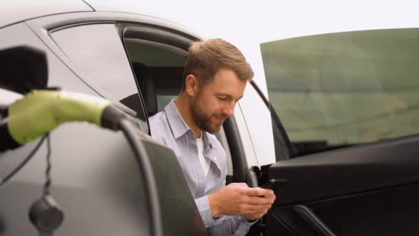 Homem Com Smartphone Esperando Acabamento Processo Carregamento Bateria Carro Elétrico — Vídeo de Stock