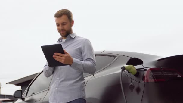 Mężczyzna Tabletem Czekający Zakończenie Procesu Ładowania Akumulatora Samochodu Elektrycznego — Wideo stockowe