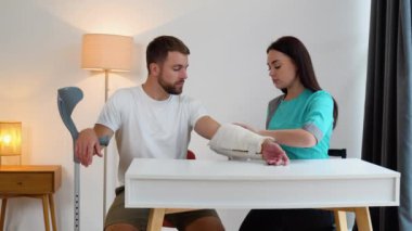 Kadın doktorun, erkek hastanın kırık ellerini sargıladığı yakın plan..