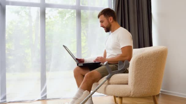 Schöner Mann Mit Gebrochenem Bein Und Arm Gips Benutzt Laptop — Stockvideo