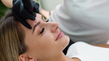 Eyebrow tattoo procedure with a permanent makeup machine.
