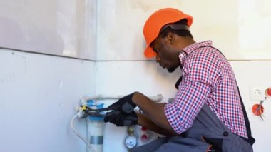 Afro-Amerikalı tesisatçı yenileme sırasında yeni bir daireye boru ve su filtresi yerleştiriyor. Yerleştirme su filtresi.