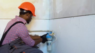 Afro-Amerikalı tesisatçı yenileme sırasında yeni bir daireye boru ve su filtresi yerleştiriyor. Yerleştirme su filtresi.