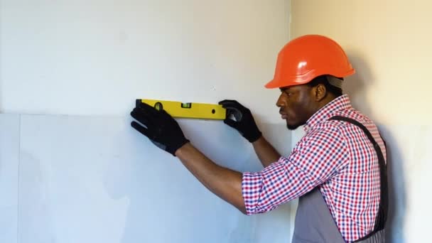 アフリカ系アメリカ人男性労働者がアパートに新しく敷かれたタイルに大工レベルを設置 — ストック動画