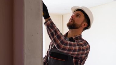 Duvarı boyayan bir işçi, sert bir şapka ve eldivenle, boya silindiri kullanıyor..