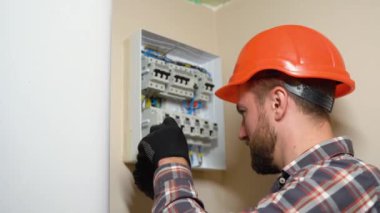 Kasketli ve ekose gömlekli profesyonel elektrikçi duvara elektrik paneli yerleştiriyor.