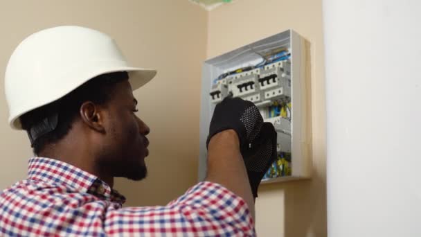 戴着硬礼帽 穿着格子呢衬衫 在墙上装上电箱的非洲裔美国专业电工 — 图库视频影像