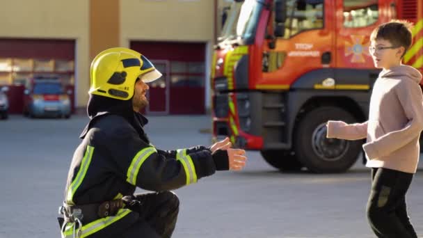 Хоробрий Пожежник Уніформі Обіймає Маленького Хлопчика Проти Пожежного Двигуна — стокове відео