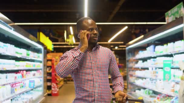 Красивий Чорний Чоловік Ходить Озирається Супермаркеті Розмовляє Телефону Своєю Дружиною — стокове відео