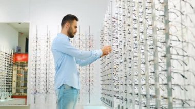 Optik dükkanında alışveriş yaparken rafın yanında duran erkek müşterinin göz giysisini seçerken yan görünümü.
