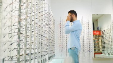 Bir adam optik dükkanında aynaya bakarak gözlük seçer..