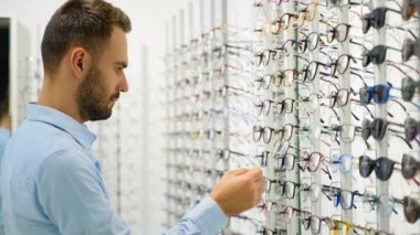 Optik dükkanında alışveriş yaparken rafın yanında duran erkek müşterinin göz giysisini seçerken yan görünümü.