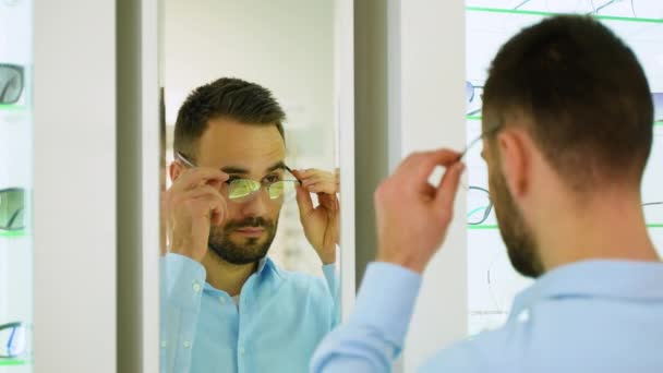 快乐的年轻男性客户戴着新眼镜 看着镜子旁边的架子和展示与眼镜 满意的客户 — 图库视频影像