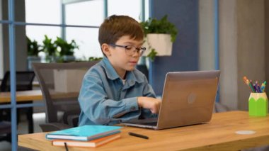 İlkokulda laptopunu kullanarak ev ödevini yapan neşeli bir öğrenci.