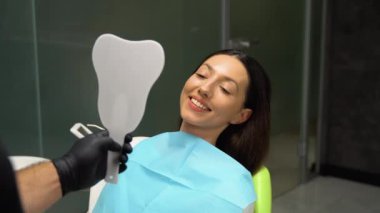 Diş beyazlatma prosedüründen sonra gülümseyen kadın aynaya bakıyor..