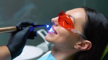 Diş sağlığı kliniğinde ultraviyole ışığı tedavi ederek diş kurutma işlemi sırasında genç bir kadın..