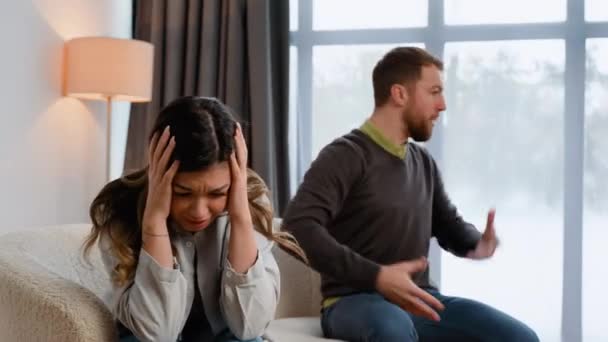 不安的妻子坐在沙发上哭泣 听着愤怒的丈夫大喊大叫 不幸的夫妇在家里吵架或争吵 — 图库视频影像