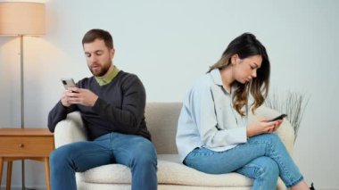 Conflict, quarrel. Man and woman, couple, family sitting on the couch with their backs to each other with phones, do not talk to each other, do not pay attention, busy with phones
