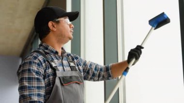 Üniformalı bir adam pencereleri kazıyıcıyla yıkıyor. Profesyonel ev ya da ofis temizleme servisi.