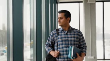 Hintli bir öğrenci okumak ve öğrenmek için bir kitap ve sırt çantasıyla üniversitede yürüyor. Yavaş çekim.