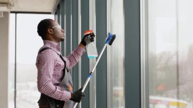 Siyah adam profesyonel temizlik işçisi ofisteki PVC pencerelerini temizliyor..