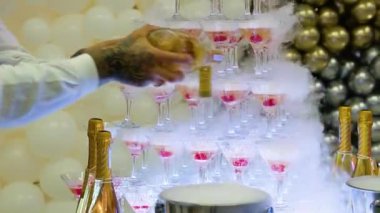 Barmen şampanya bardaklarını dolduruyor. Düğün partisinde kulede duran şampanya kadehleri. Şampanya cam piramidi.
