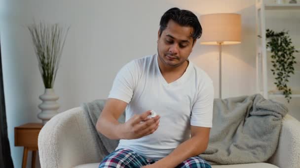 インドの男性はソファーに座っている間鼻スプレーをスプレーします ウイルス性疾患の概念 — ストック動画