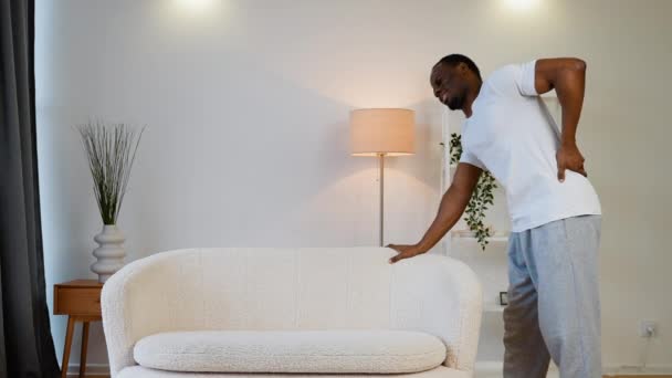 Hombre Afroamericano Con Dolor Espalda Mientras Mueve Tratando Levantar Sofá — Vídeo de stock