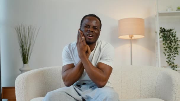 歯痛のために痛い表情で手で口に触れる自宅の黒人の男 — ストック動画
